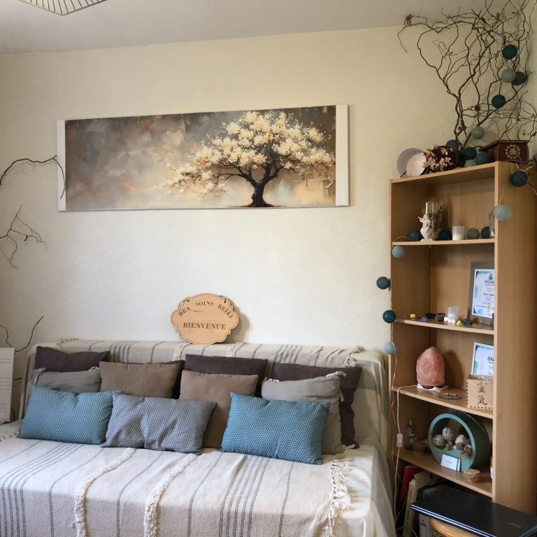 Lit cocooning avec coussins et plaid, sous une peinture d'arbre en fleurs et un panneau en bois « Bienvenue »