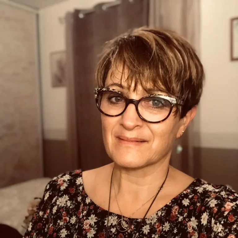 Mon Portrait Femme avec des lunettes, cheveux courts et châtain, souriant dans une pièce lumineuse.